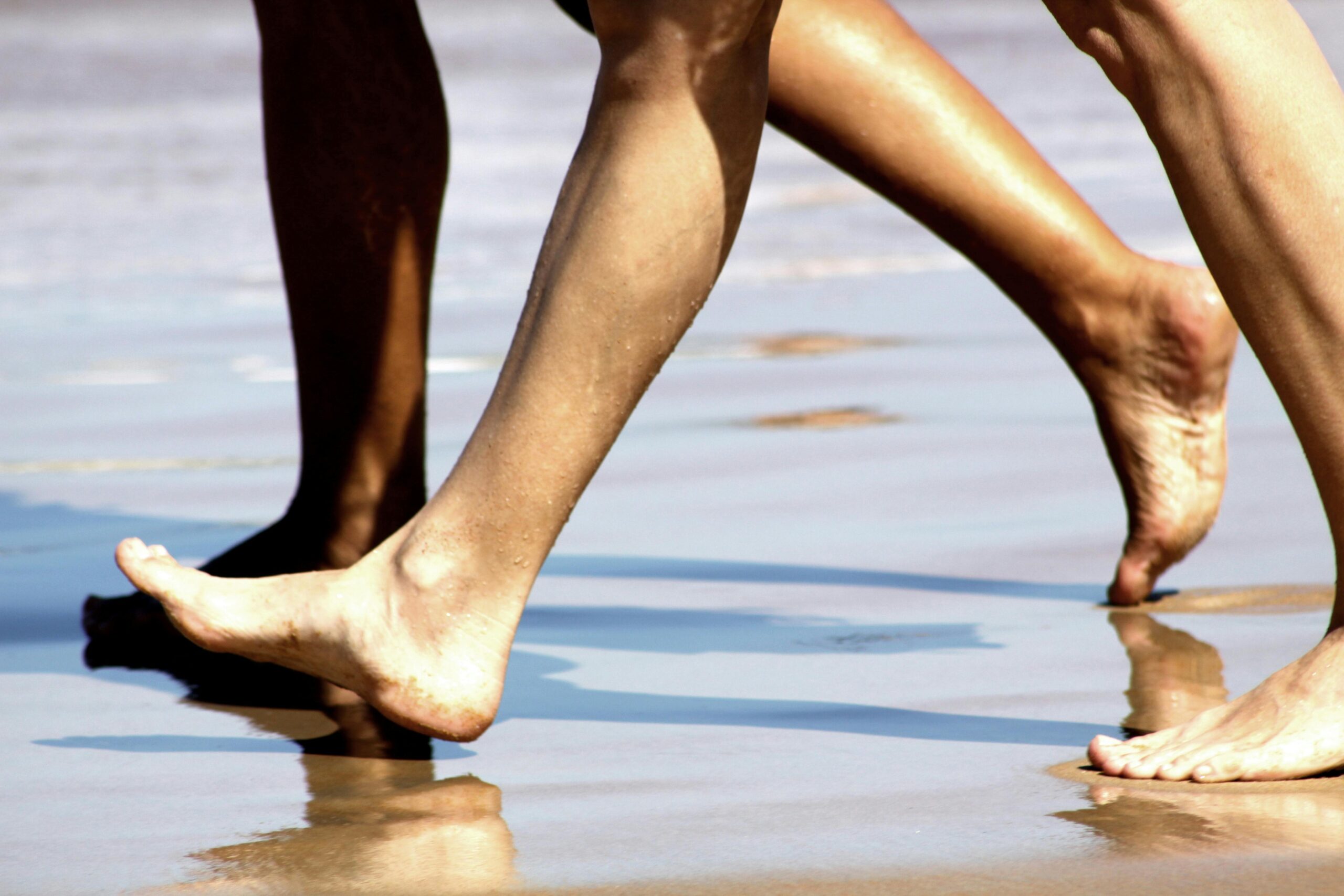 Nahaufnahme nackter Füße beim Laufen auf dem nassen Sand des Strandes von Búzios, ein Ausdruck sommerlicher Entspannung.
