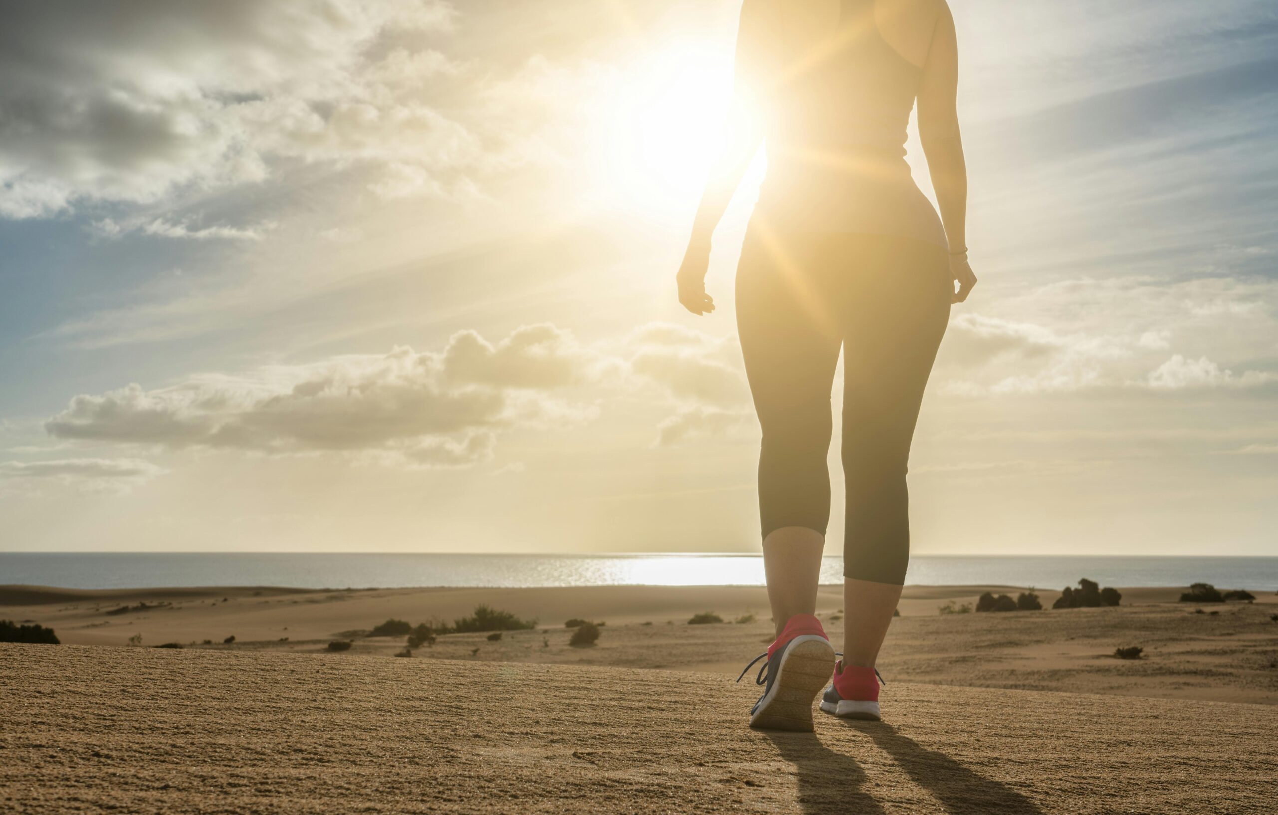 Eine Frau geht bei Sonnenuntergang an einem Sandstrand zum Meer und strahlt Einsamkeit aus.