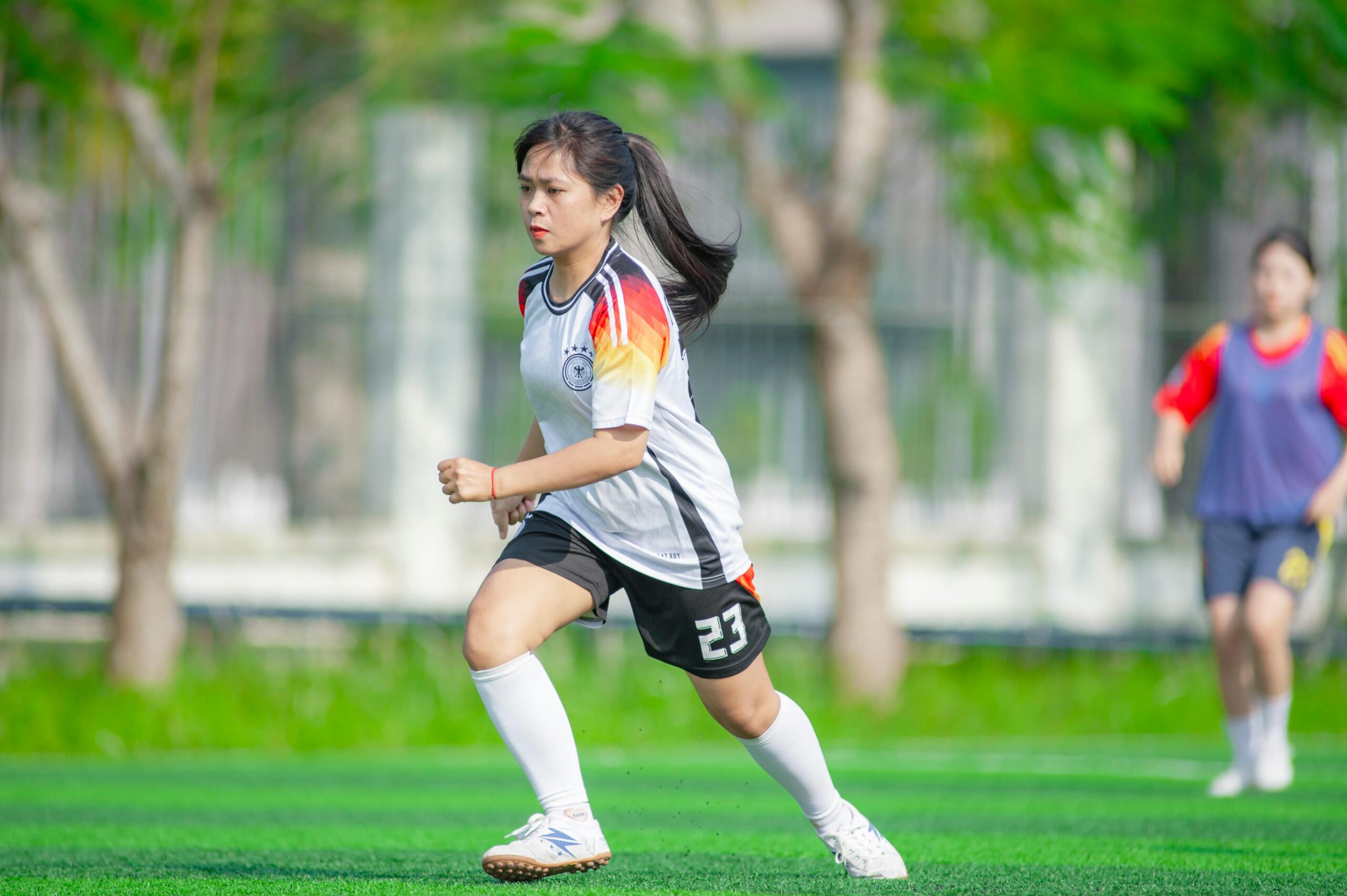 Eine junge Frau in Fußballtrikot spielt auf einem leuchtend grünen Feld in Hanoi, Vietnam.