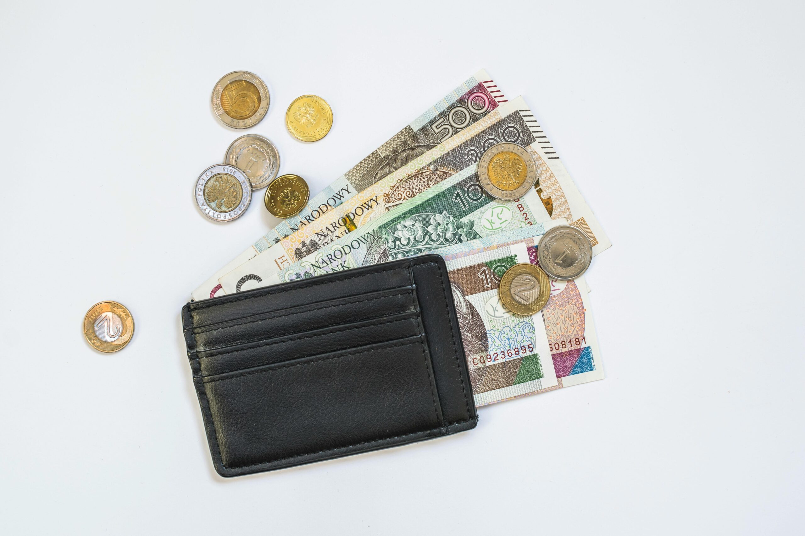 Flache Lage polnischer Zloty-Banknoten und -Münzen mit einer schwarzen Brieftasche auf weißem Hintergrund.