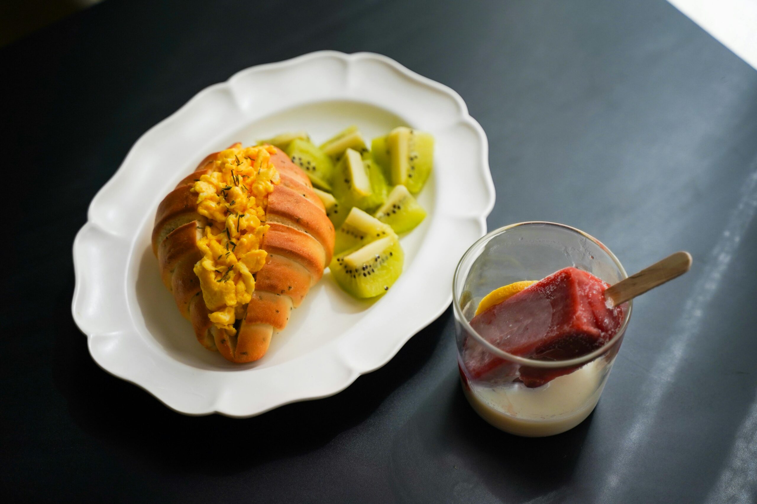 Leckeres Frühstück mit gefülltem Croissant, frischer Kiwi und Dessert auf einem Teller.