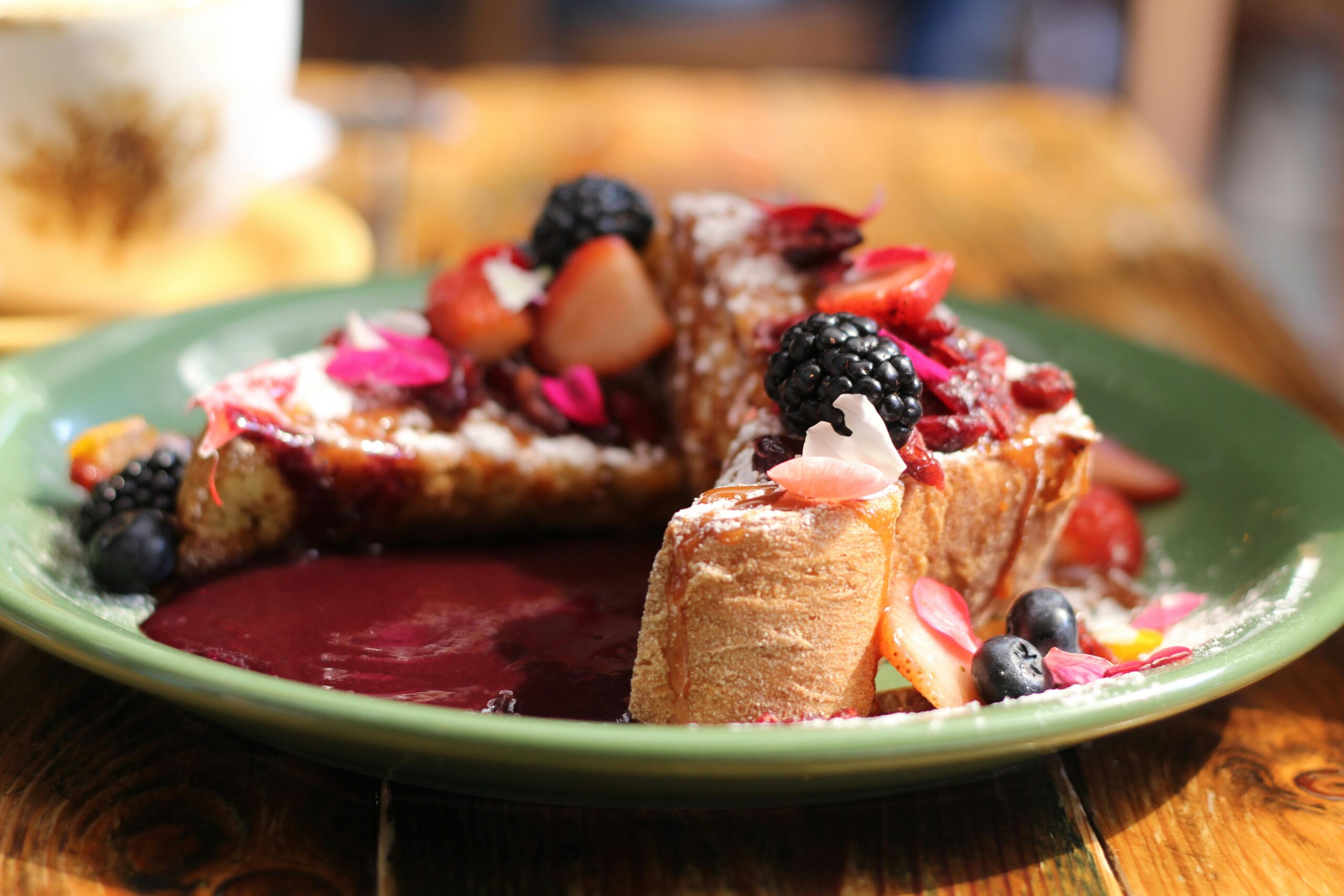 Leckerer French Toast mit frischen Beeren und Sirup auf einem grünen Teller.