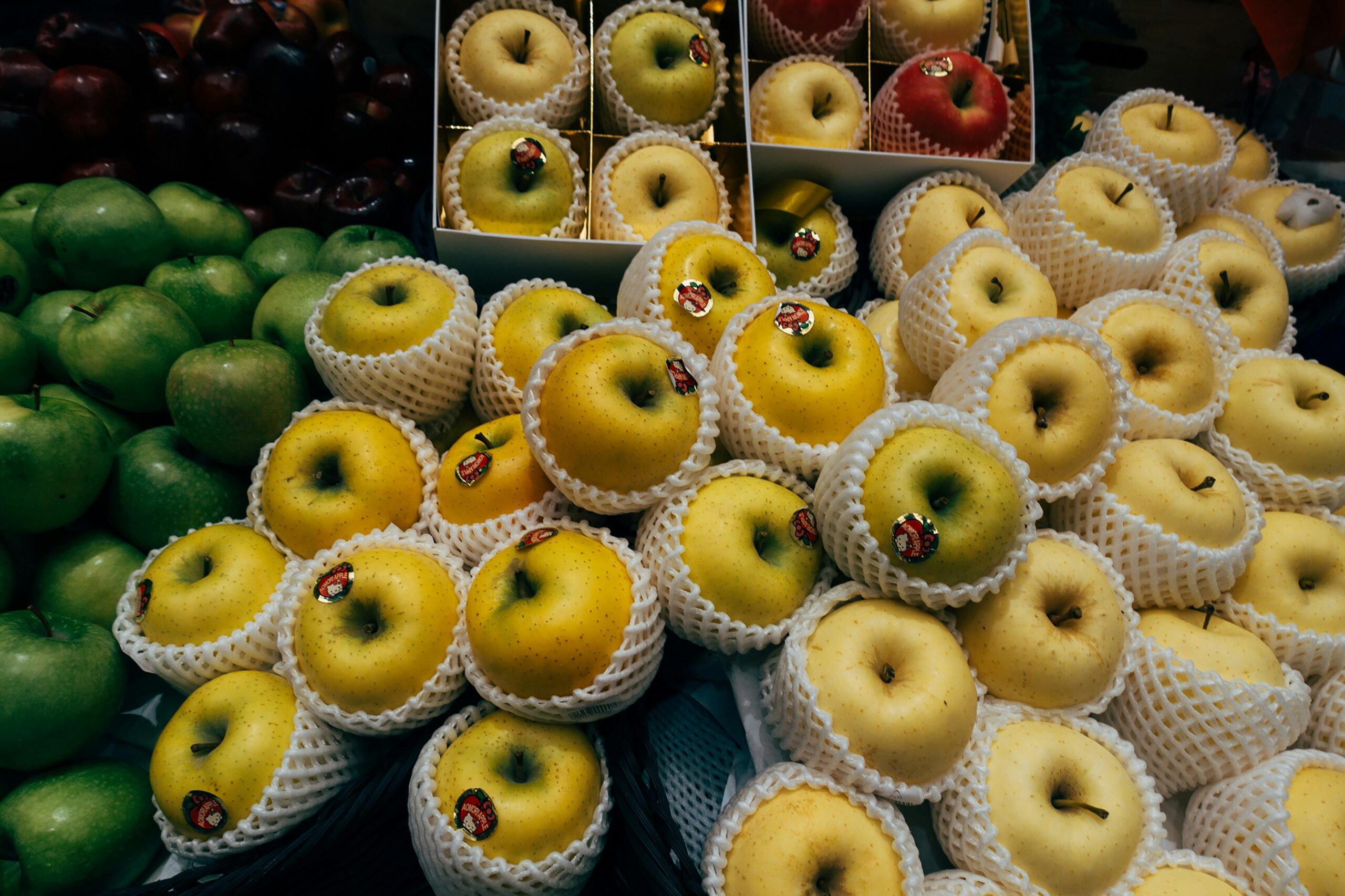 Eine farbenfrohe Auslage mit grünen, gelben und roten Äpfeln mit Schutznetzen auf einem Markt.