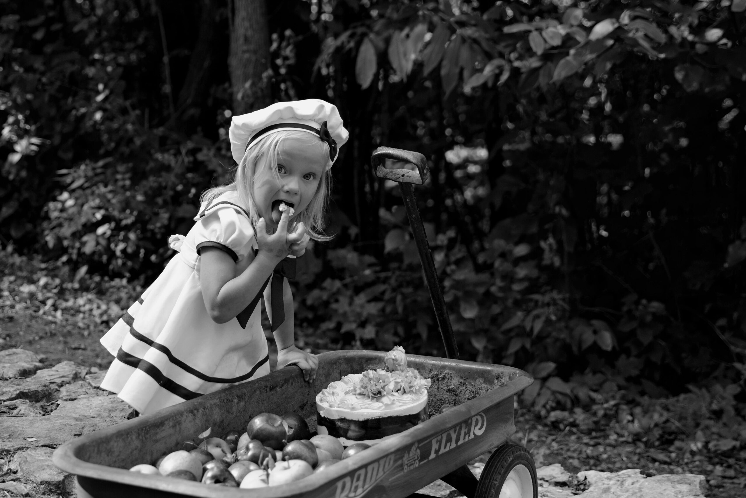 Ein junges Mädchen beißt in einem Wald neben einem Wagen voller Erzeugnisse in einen Apfel.