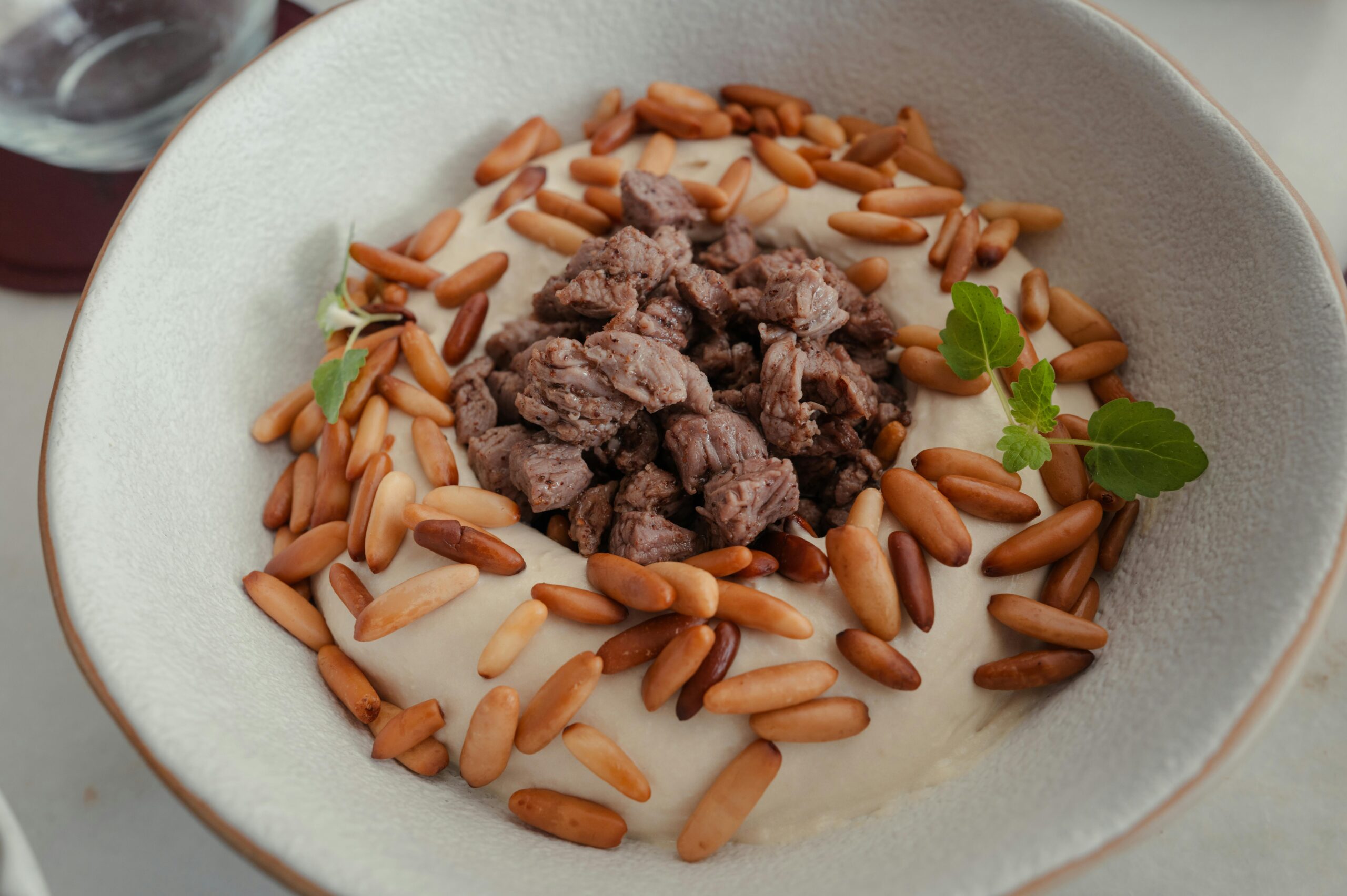 Leckere Hummus-Schüssel mit gewürztem Rindfleisch und gerösteten Pinienkernen, garniert mit frischen Kräutern.
