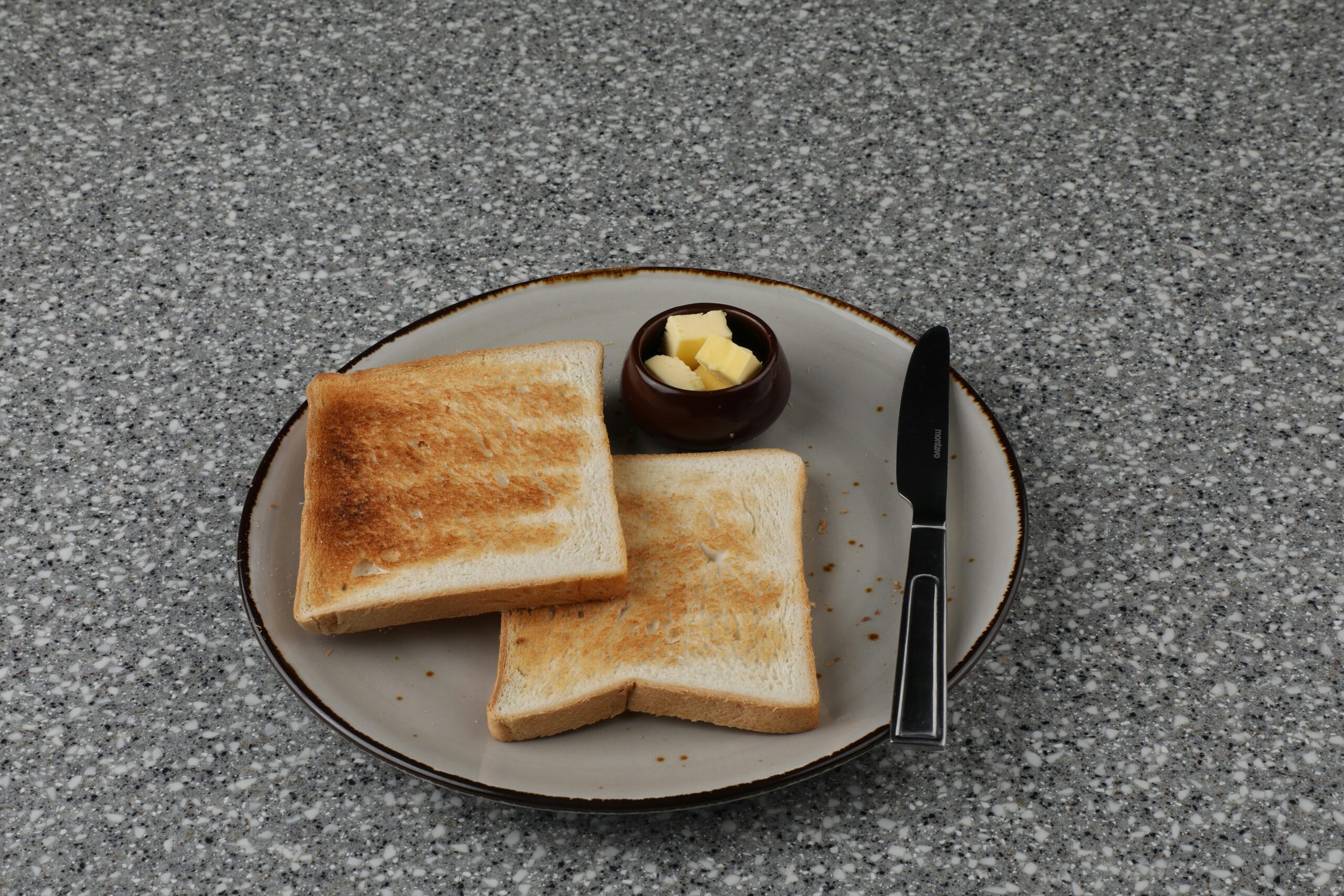 Zwei Scheiben geröstetes Brot mit Butter auf einer grauen Tischoberfläche.