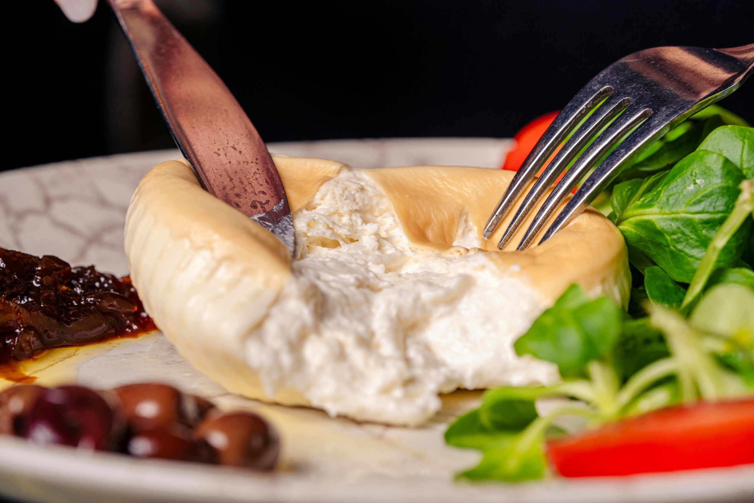 Nahaufnahme von cremigem Käse, serviert mit Salat, Oliven und sonnengetrockneten Tomaten.