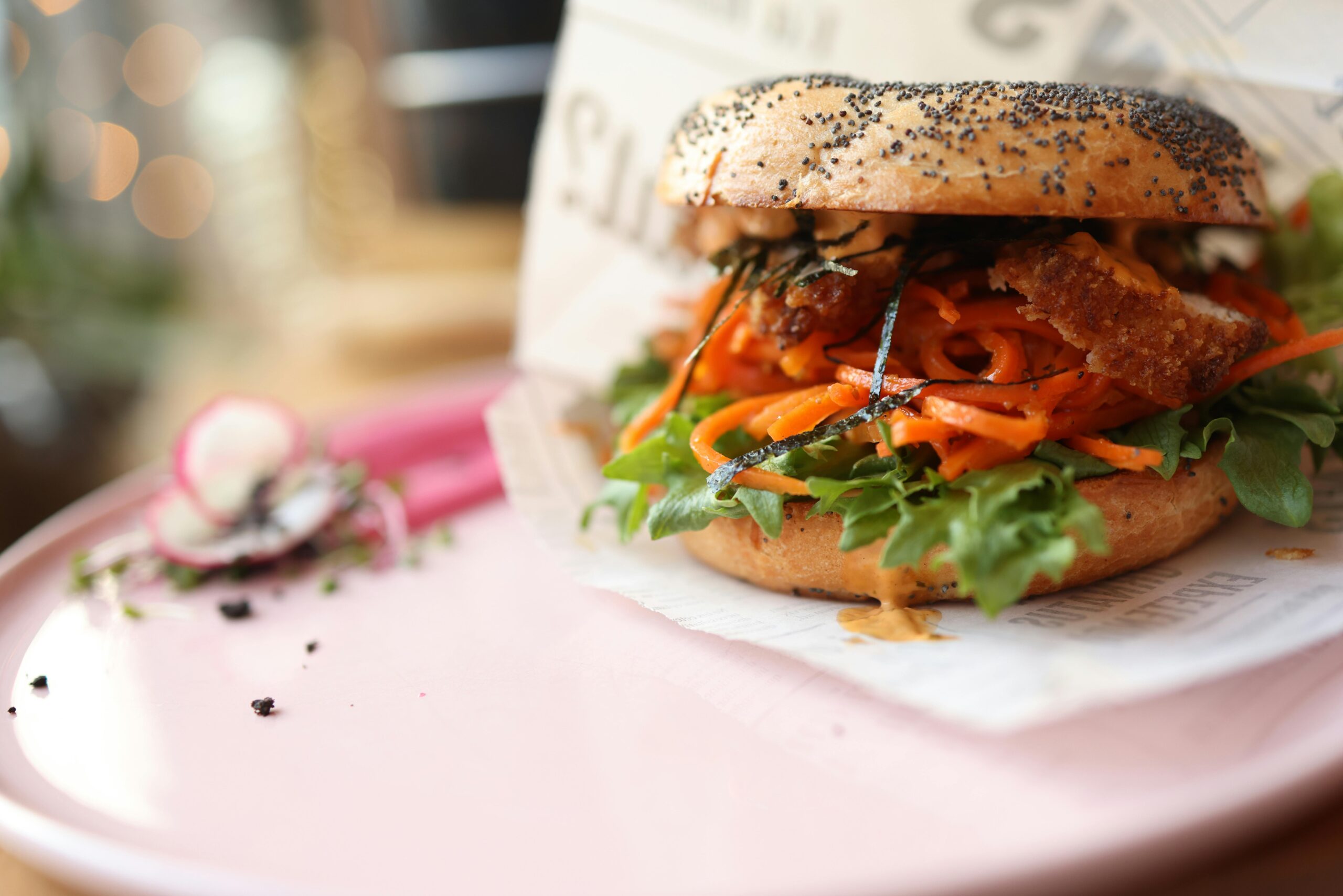 Nahaufnahme eines Gourmet-Bagel-Sandwiches mit Gemüse auf einem rosa Teller, perfekt für Feinschmecker.