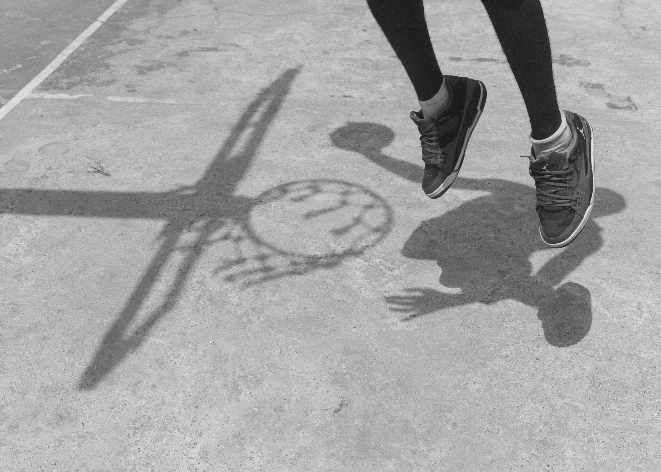 Schwarzweißfoto, das einen Sprung auf einem Basketballplatz im Freien mit Schuhschatten festhält.