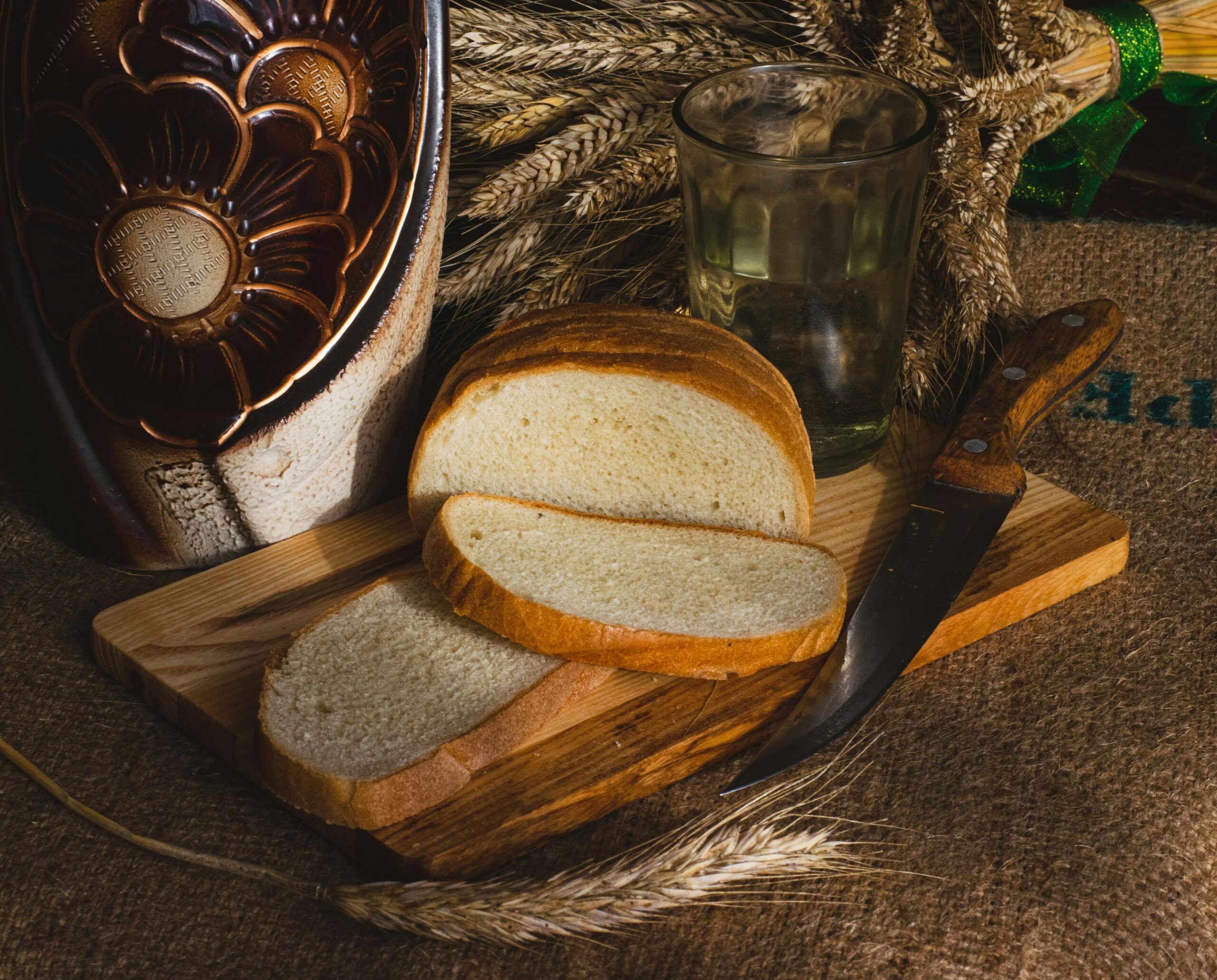 In Scheiben geschnittenes selbstgebackenes Brot mit Messer auf Holzbrett, rustikales Stillleben mit Weizenhalmen.