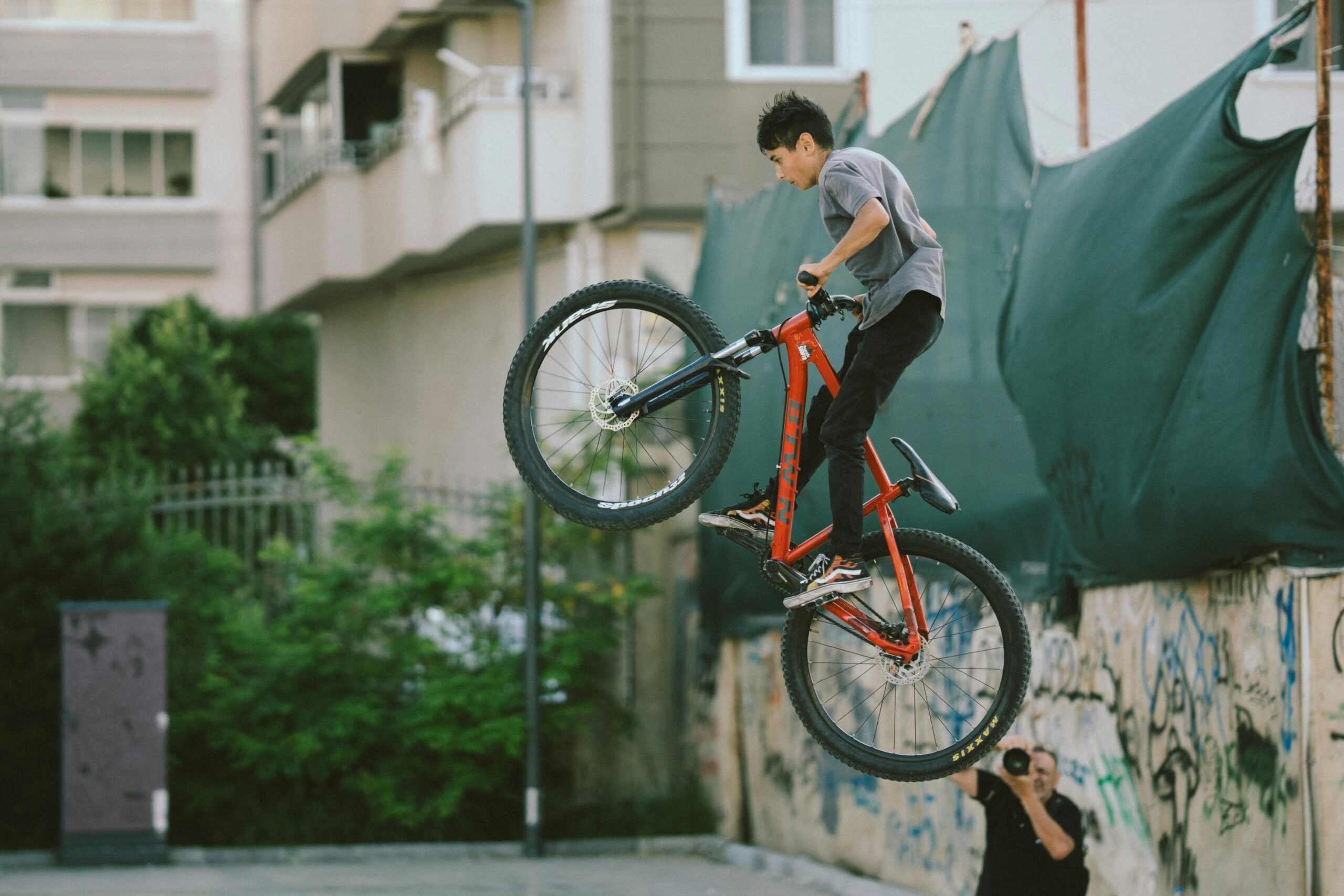 Ein Biker führt mit einem roten Mountainbike in einer mit Graffiti übersäten städtischen Umgebung einen beeindruckenden Stunt durch.