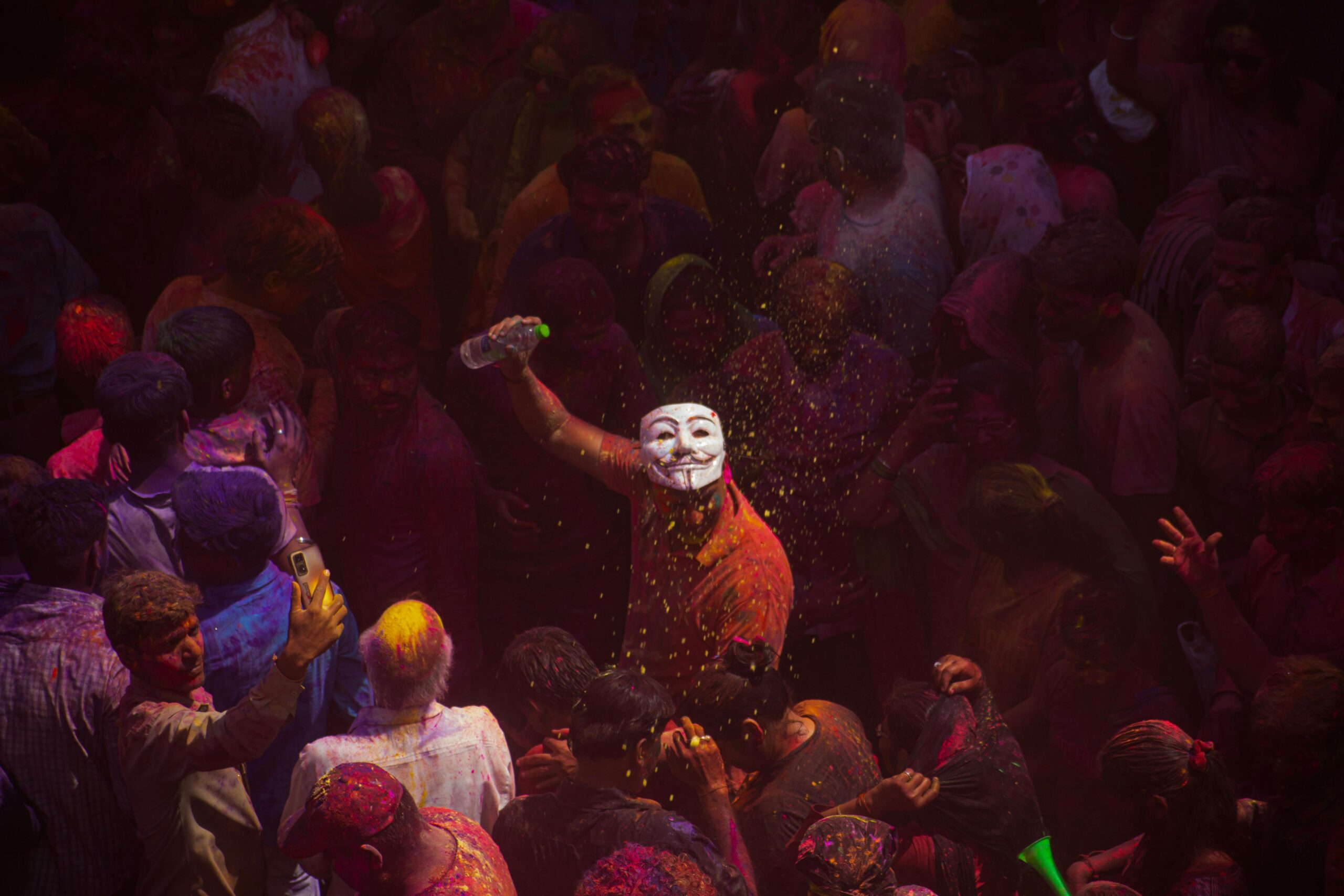 Farbenfrohe Feier während des Holi-Festes mit einer Anonymous-Maske in einer lebhaften Menge.
