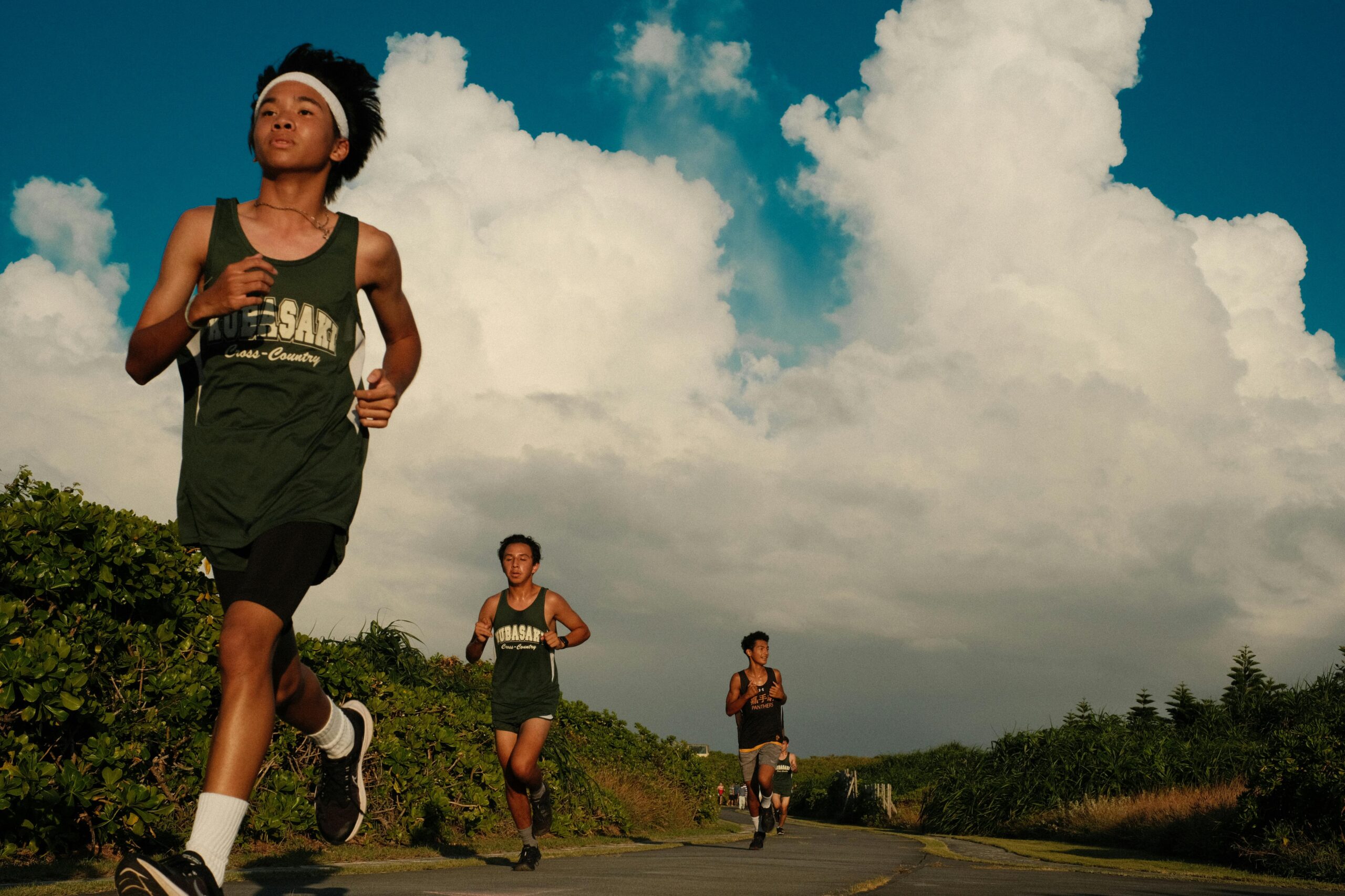 Drei Teenager joggen an einem sonnigen Tag mit dramatischen Wolken im Hintergrund. Perfekt für Fitness- und Lifestyle-Themen.