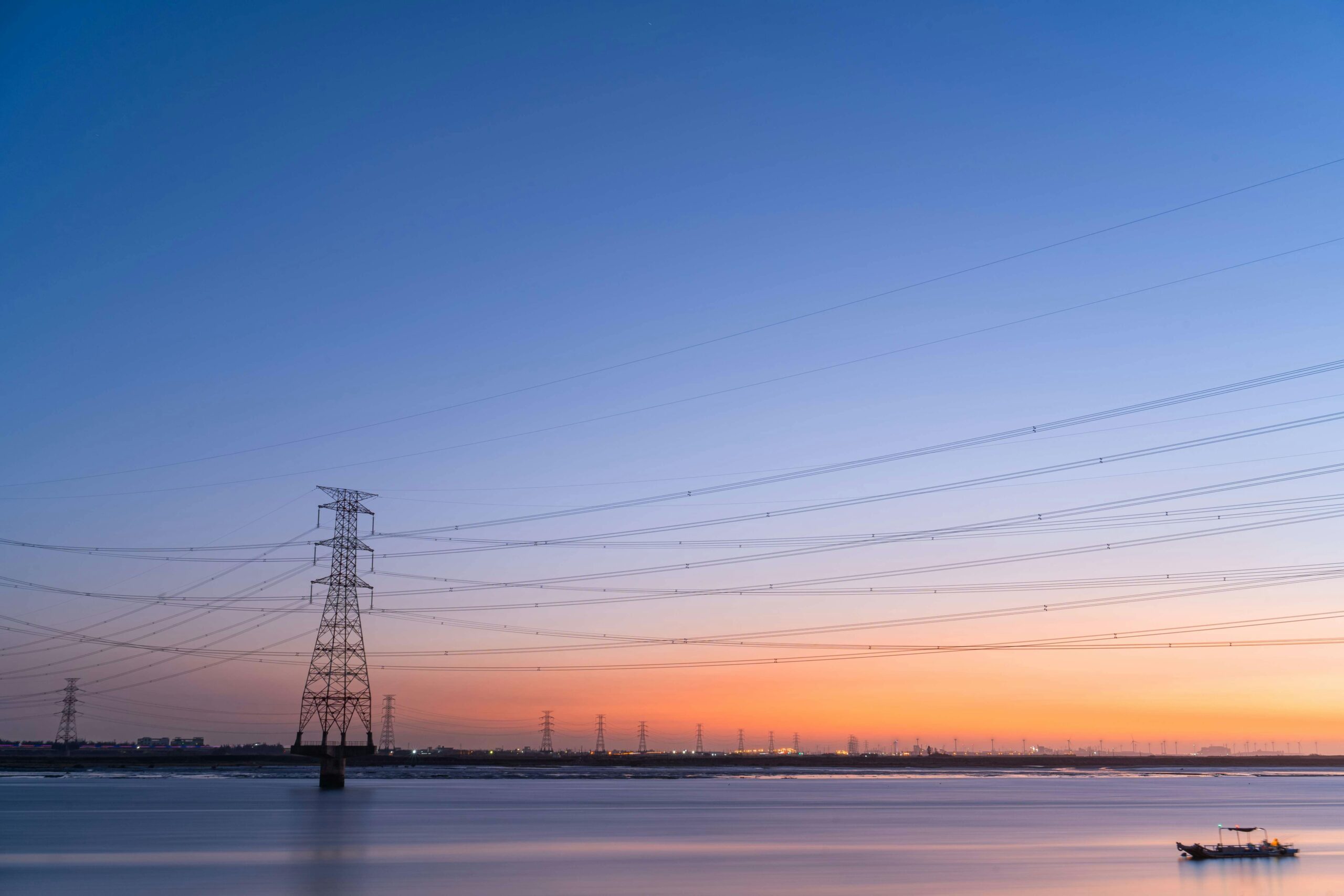 Atemberaubender Sonnenuntergang über einem ruhigen Fluss mit hoch aufragenden Stromleitungen in Taiwan, farbenfroher Himmel.