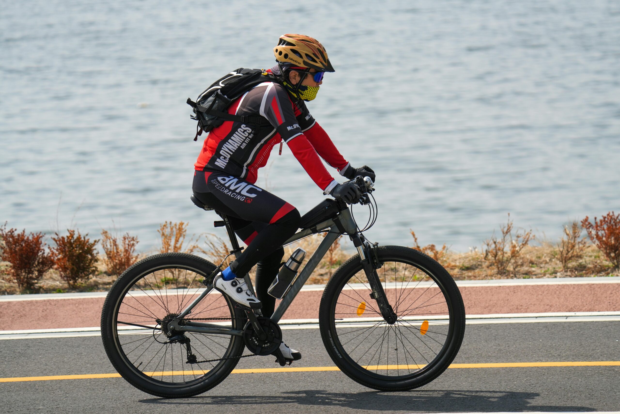 Ein Radfahrer in Schutzausrüstung fährt an einem sonnigen Tag am Wasser entlang und zeigt so, wie man sich gesund im Freien bewegt.
