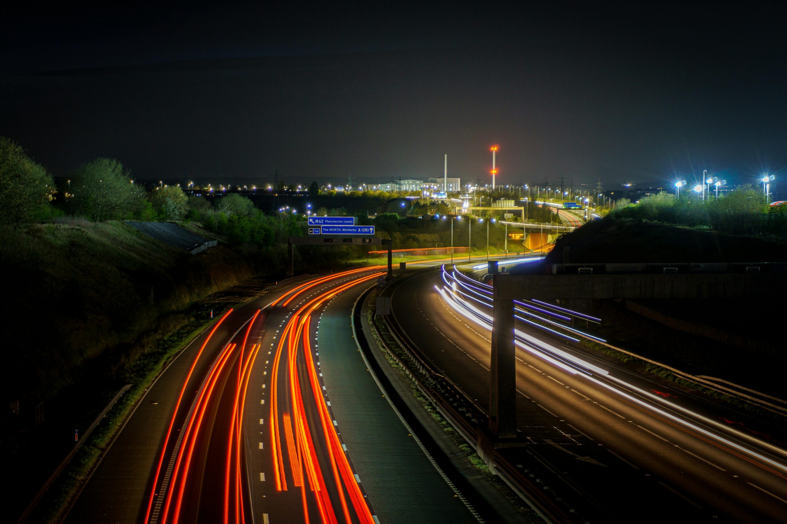 Langzeitbelichtungsaufnahme einer britischen Autobahn bei Nacht mit leuchtenden Lichtspuren vorbeifahrender Autos.