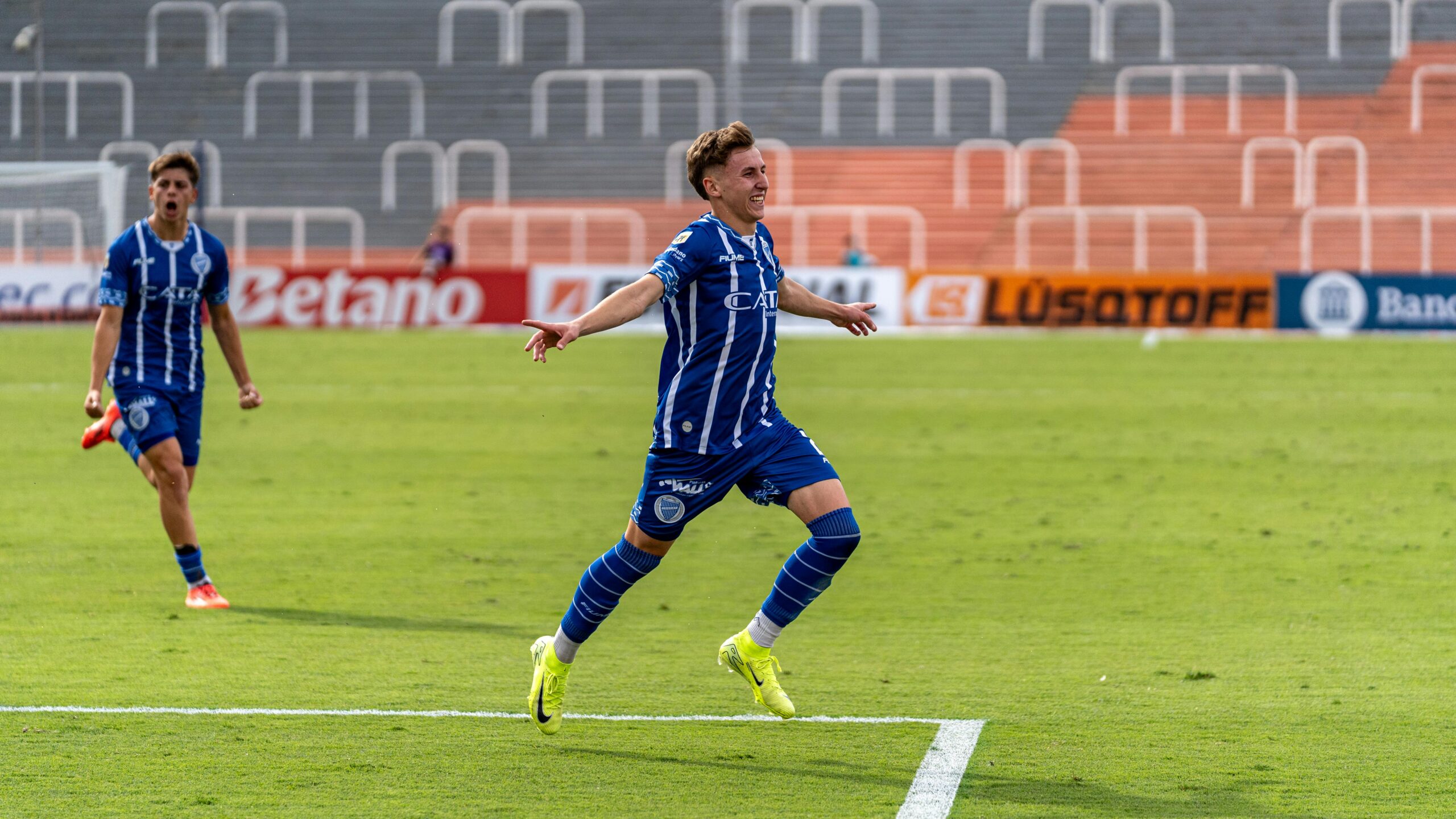 Zwei Fußballspieler in blauen Uniformen feiern ein Tor auf dem Spielfeld.