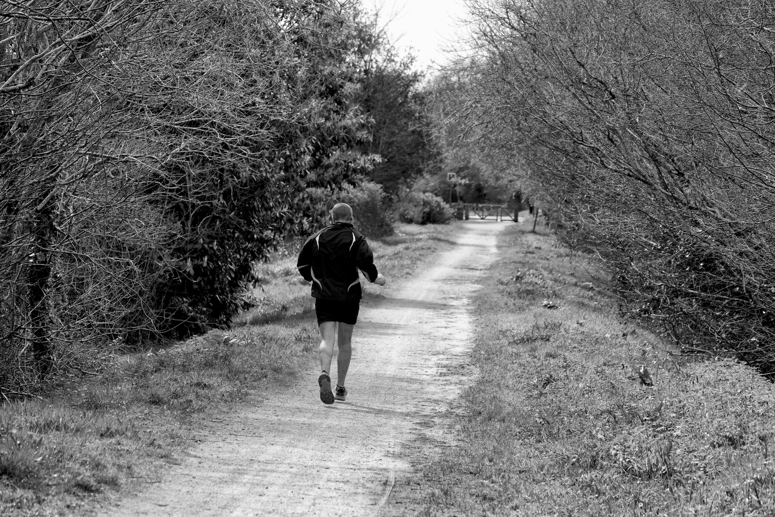 Erwachsener lÃ¤uft auf einem Waldweg in einer schwarz-weiÃŸen Umgebung und zeigt Fitness im Freien und Natur.